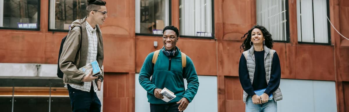 Three diverse smiling students standing on university campus. Free Universities in America