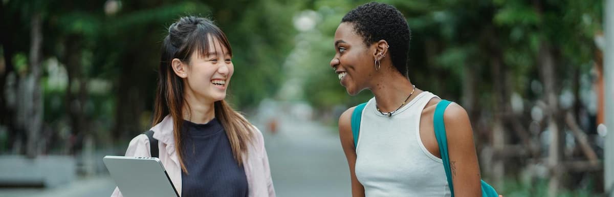 An asian female student and a Black female student share a laugh as they walk on the road. Best Student Health Insurance for Studying in Australia: 2026 OSHC Guide